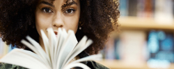Color photo of a young woman whose face is obscured by an open book
